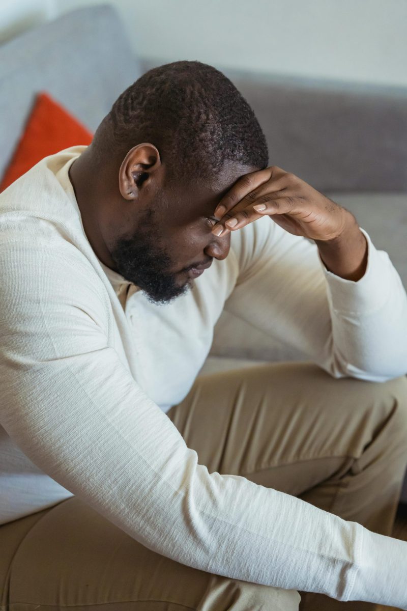Side view of a pensive man sitting indoors, expressing stress and fatigue.